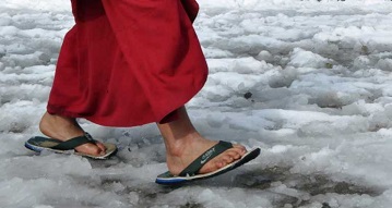 Тибетский монах идет в сланцах по снегу